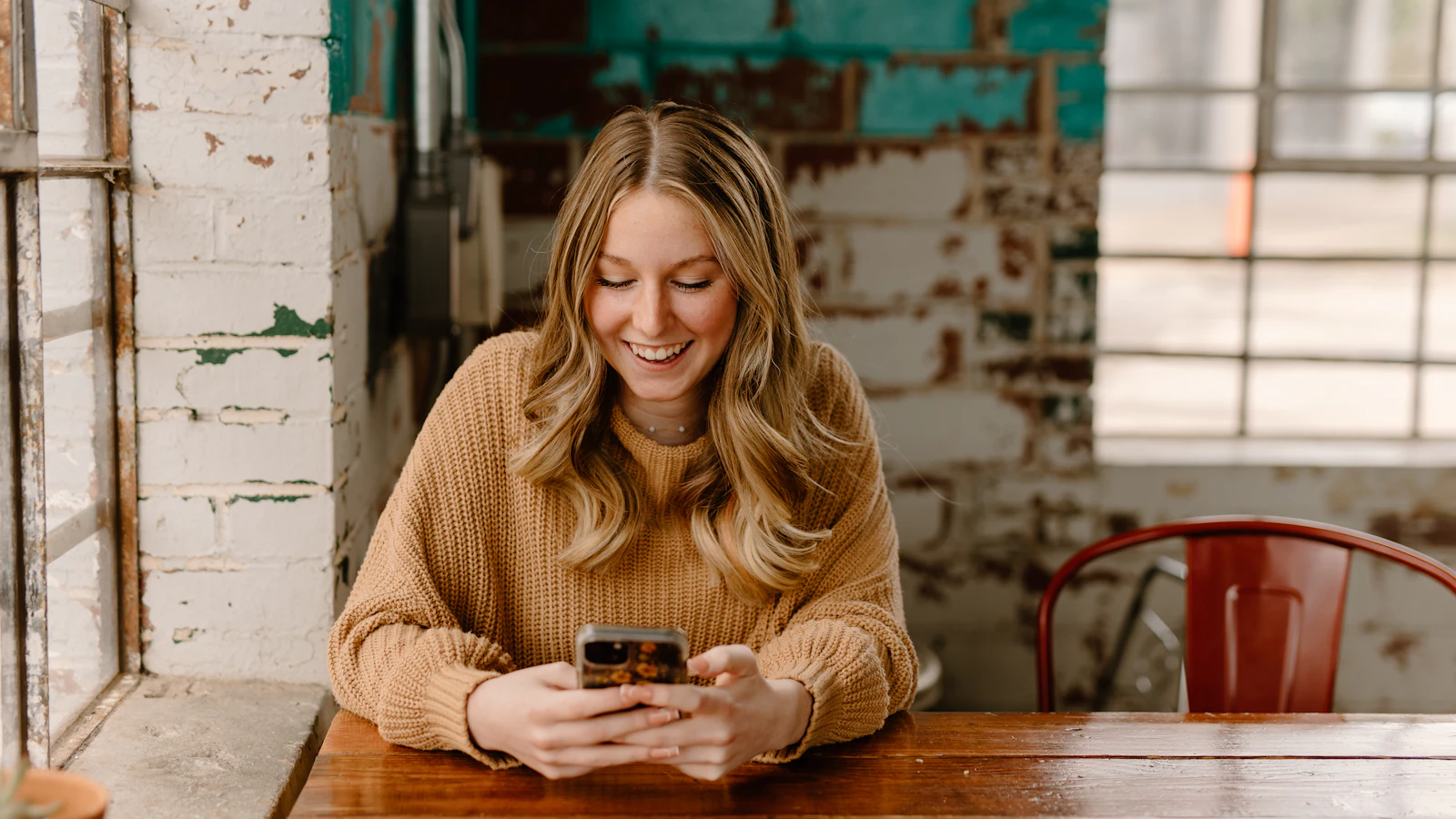 Woman at a coffee shop table looking up a local business on her phone